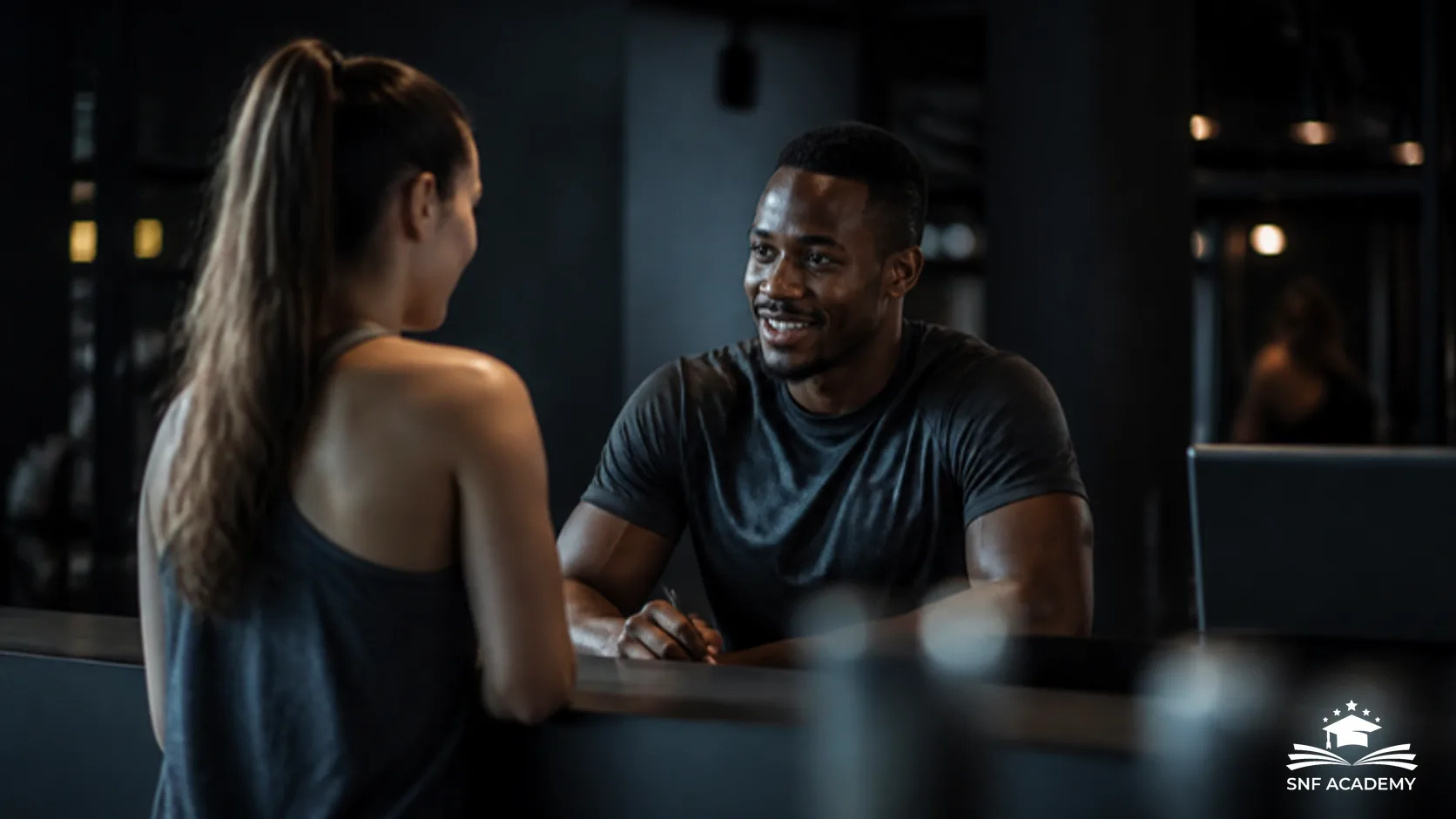 Trainer im Gespräch mit einer neuen Kundin am Empfang eines Fitnessstudios