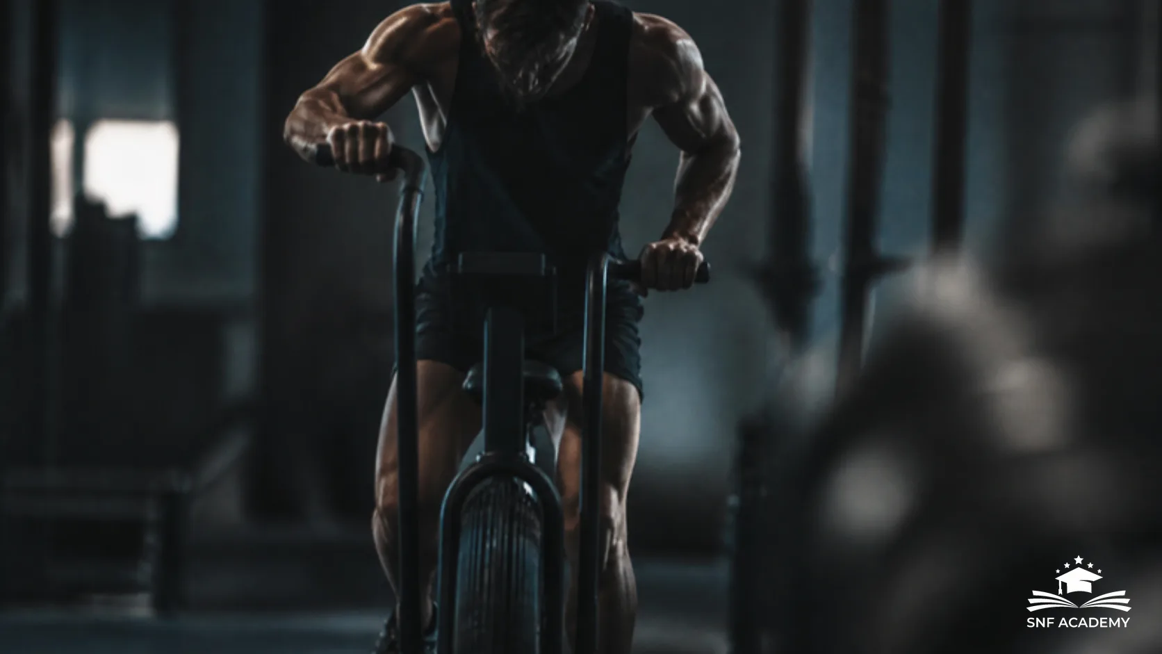 Sportler im Intervalltraining auf einem Air Bike in einem dunklen Fitnessstudio