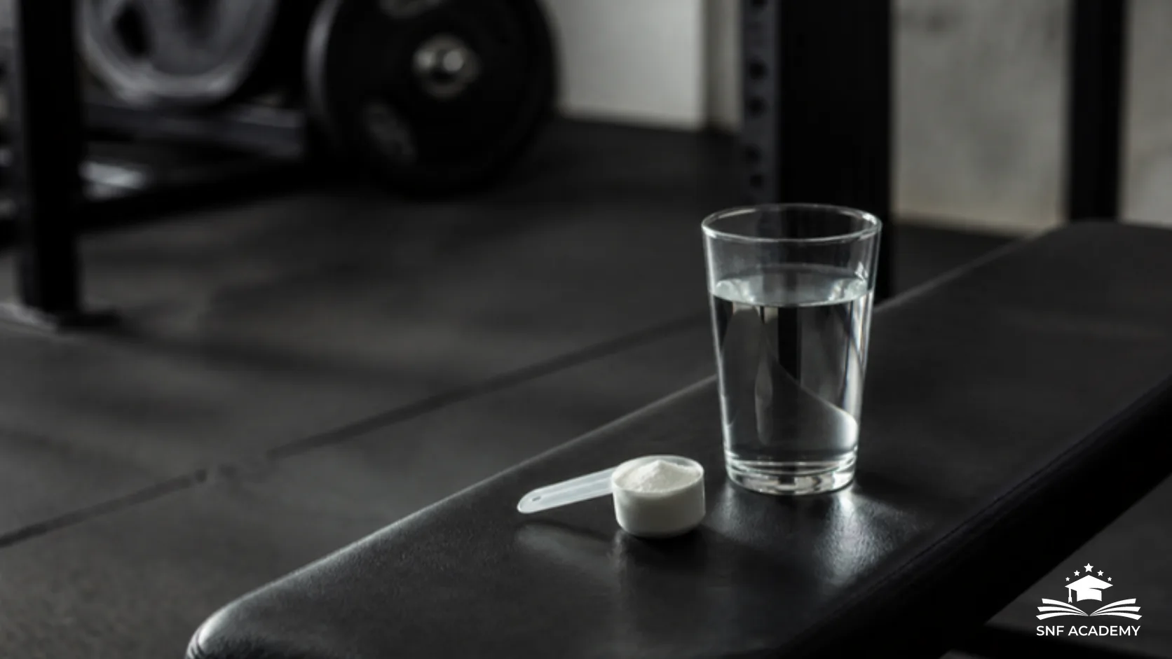 Wasserglas und Messlöffel mit weissem Pulver auf einer Hantelbank im Trainingsraum