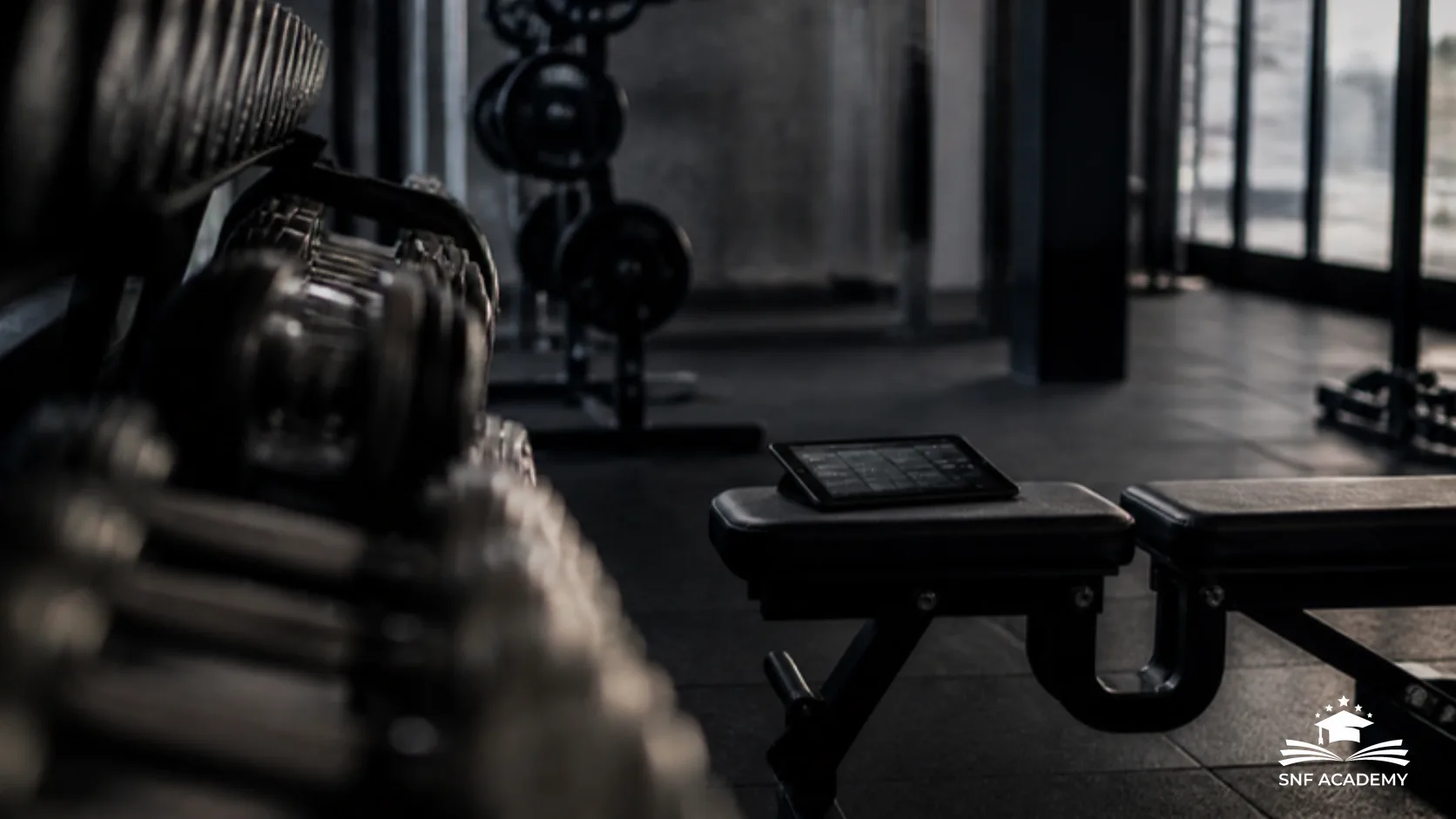 Tablet auf einer Trainingsbank in einem abgedunkelten Studio zwischen Hanteln