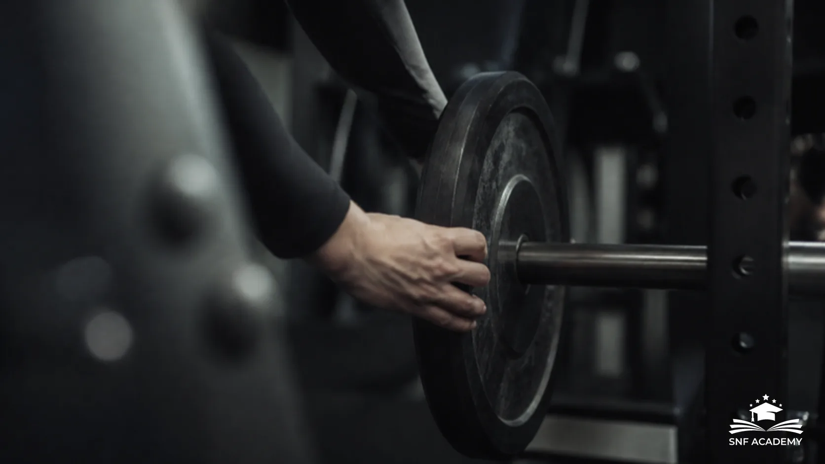 Hände laden eine Gewichtsscheibe auf eine Langhantel im dunklen Fitnessstudio