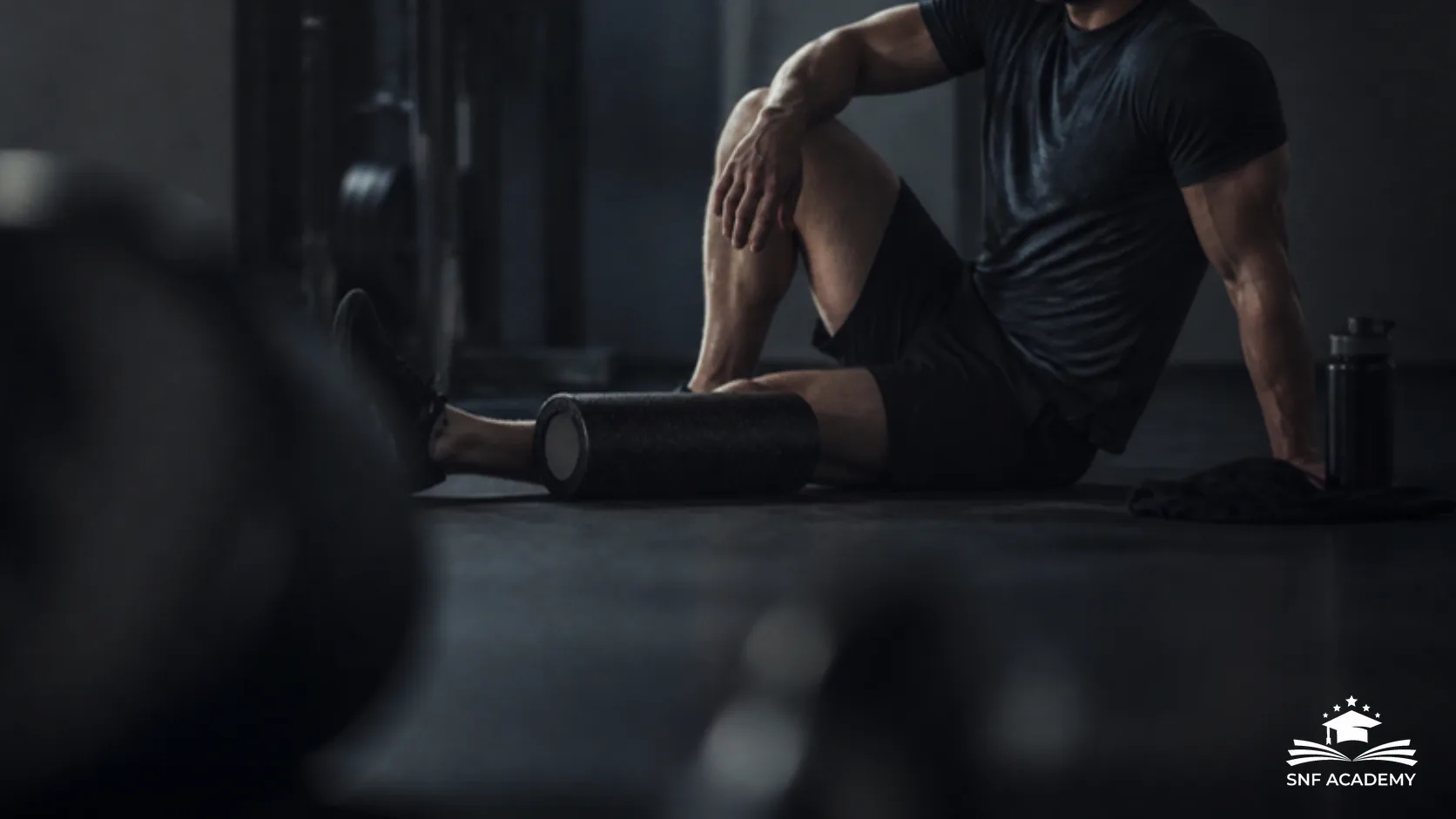 Sportler erholt sich mit Faszienrolle und Handtuch auf dem Boden eines dunklen Fitnessstudios