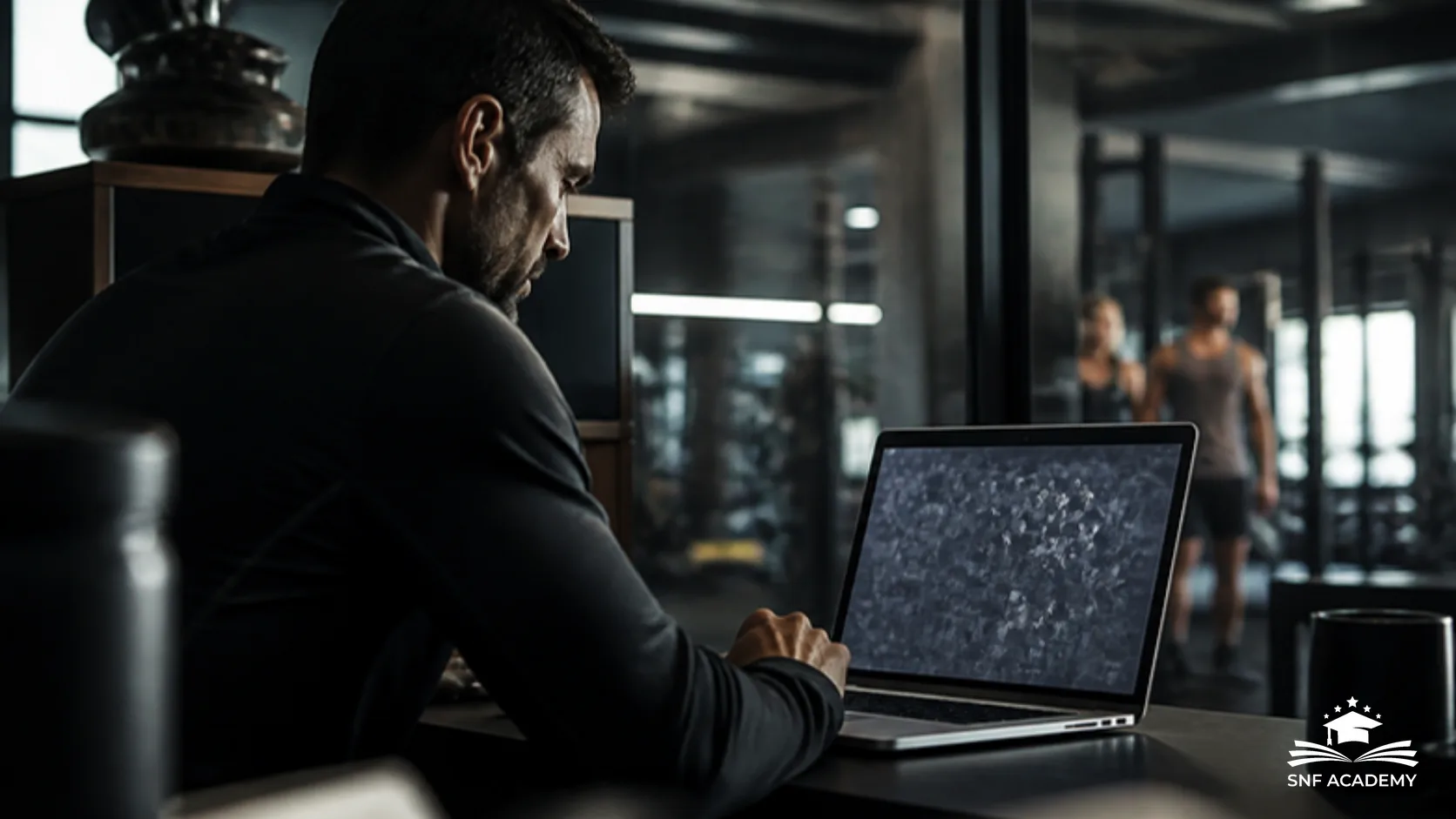 Fitnessstudio-Inhaber arbeitet im Büro am Laptop mit Blick auf die Trainingsfläche