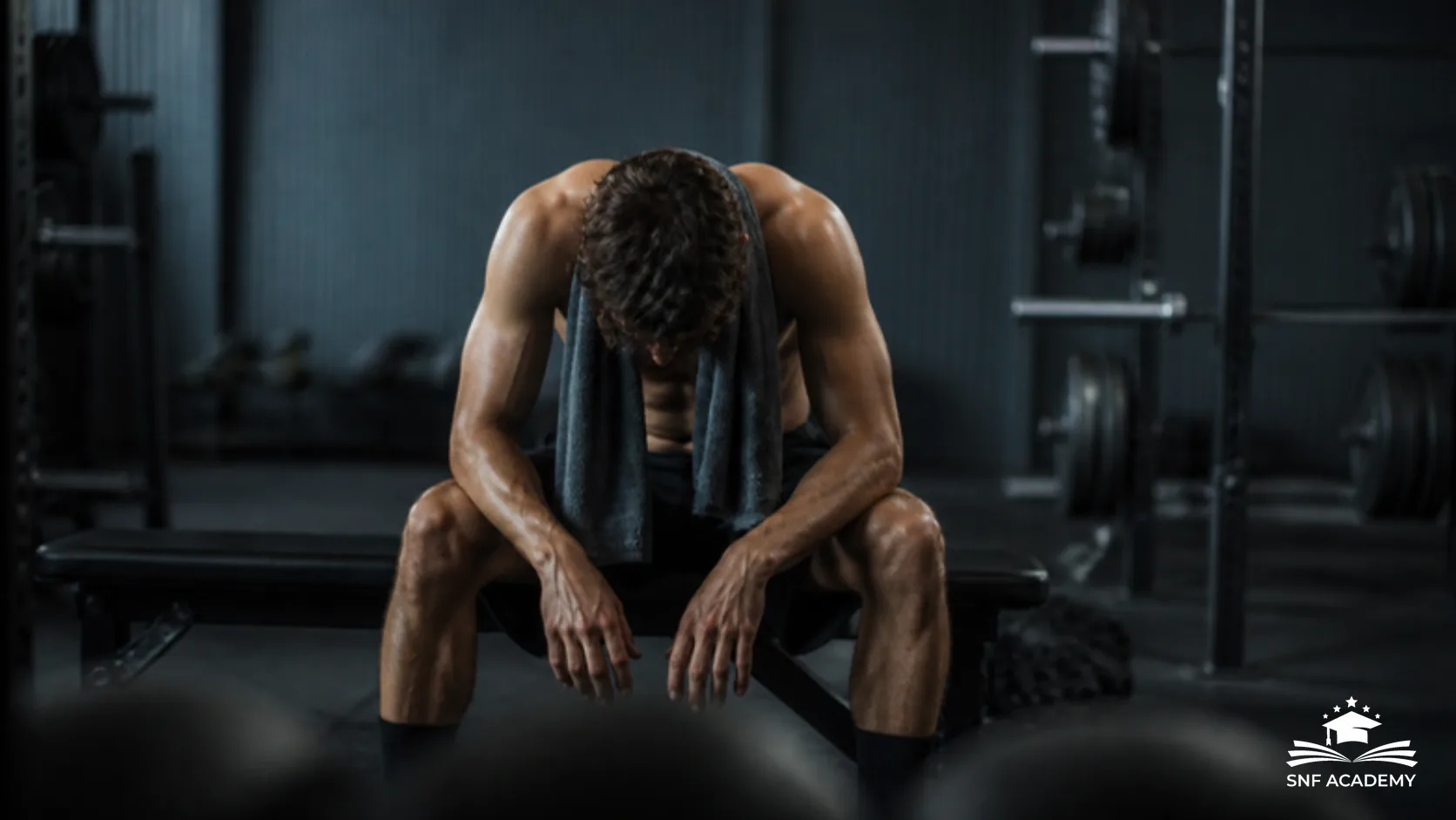 Erschöpfter Sportler sitzt mit gesenktem Kopf auf einer Bank im Fitnessstudio