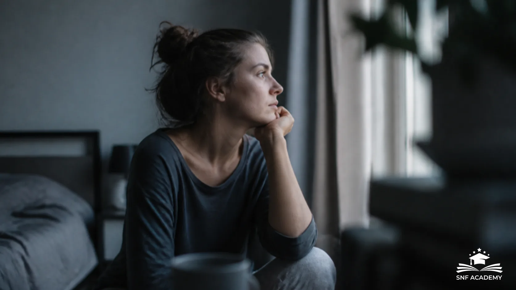 Frau sitzt am Morgen müde am Fenster im Tageslicht, Symbolbild für Beschwerden bei Vitamin-D-Mangel