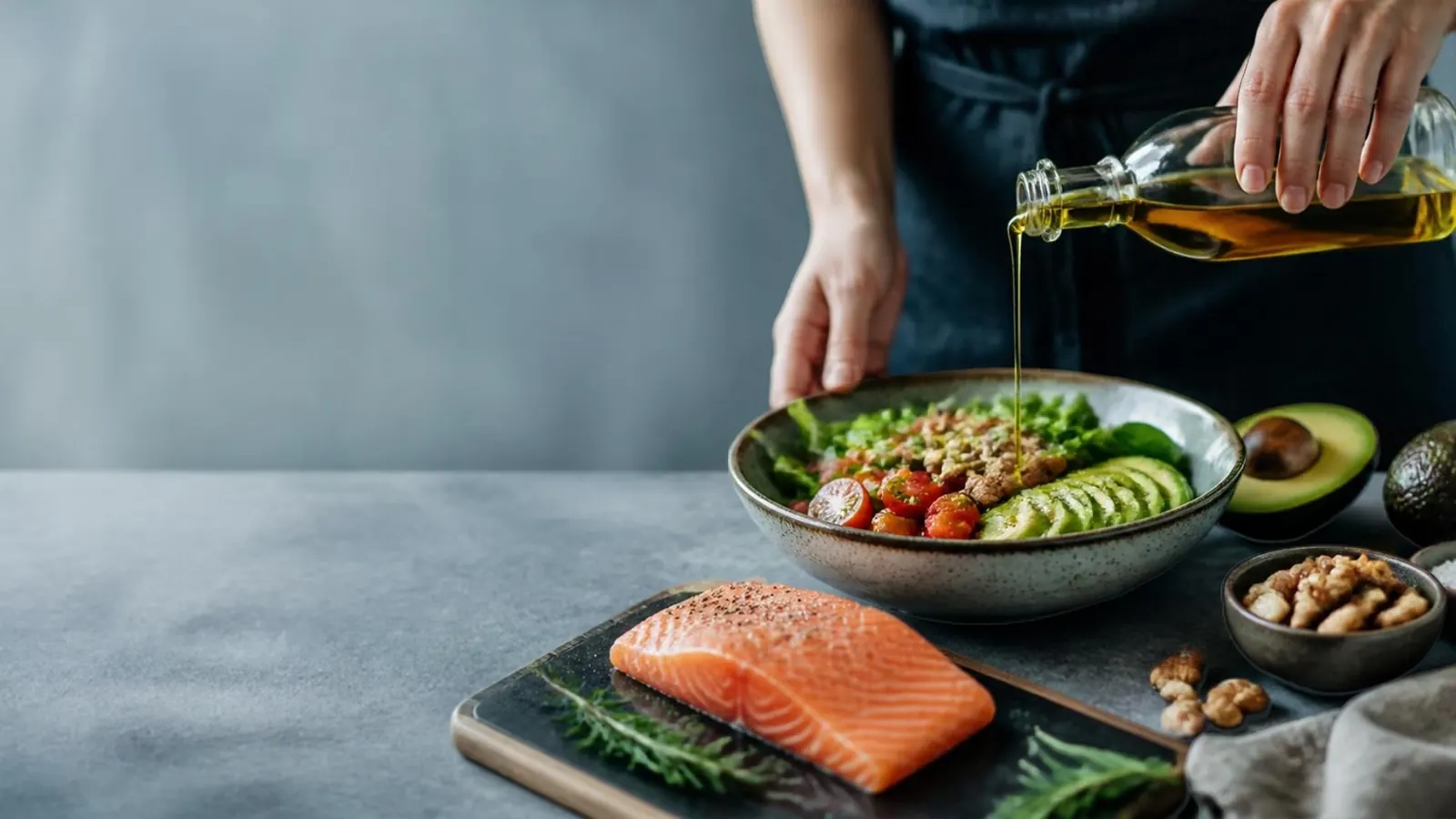 Gesunde Fette: Olivenöl, Lachs und Avocado Olivenöl wird über eine Bowl mit Avocado gegossen, daneben frischer Lachs